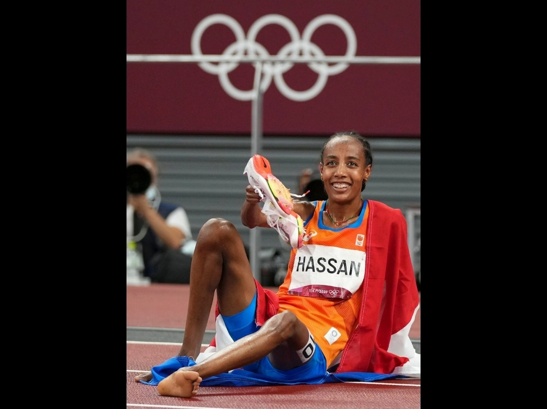 La campeona olímpica muestra feliz sus zapatillas "voladoras" luego de cruzar la meta sobre la pista mojada por la lluvia, el 2 de agosto de 2021. Foto Ap