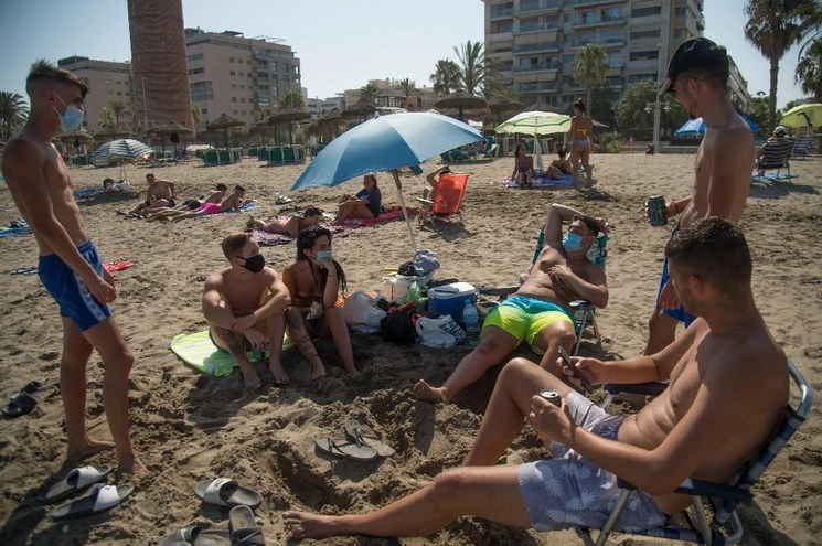 Personas con y sin cubrebocas toman el sol en la playa de La Misericordia, en Málaga, España. Foto Afp
