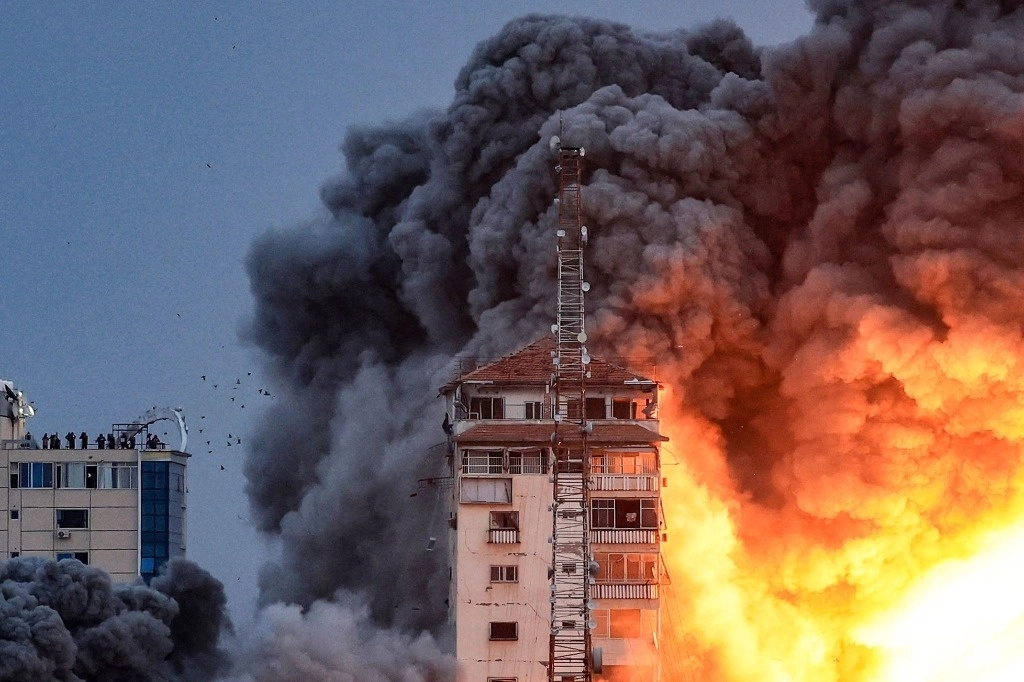 Personas paradas en una azotea observan cómo una bola de fuego y humo se eleva sobre un edificio en la ciudad de Gaza el 7 de octubre de 2023. Foto Afp