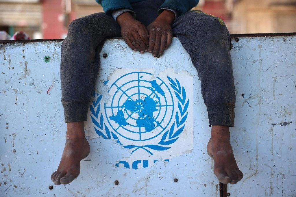 Un niño palestino permanece sentado justo en donde se encuentra pegada una imagen del logo de las Naciones Unidas, en el centro de la Franja de Gaza, este 2 de diciembre de 2024, en medio de la guerra en curso entre Israel y los militantes de Hamás. Foto AFP 
