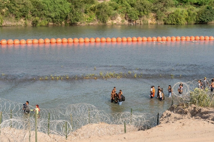 Migrantes caminan junto a una serie de boyas colocadas en el agua a lo largo de la frontera de río Bravo con México, en Eagle Pass, Texas, el 2 de agosto de 2023. Foto Afp