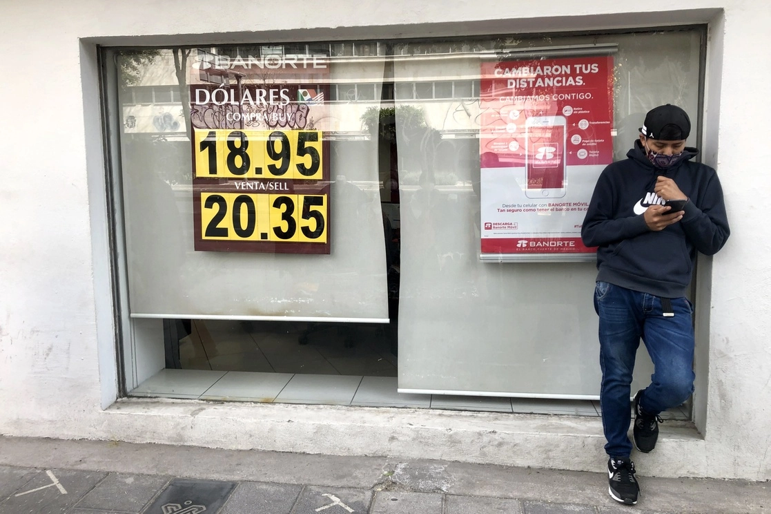 Un hombre revisa su celular frente a una sucursal bancaria en la CDMX. Foto Luis Castillo