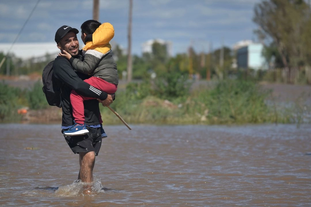 Un hombre con un niño camina por las aguas inundadas el día después de una fuerte tormenta en Bahía Blanca, 600 km al sur de Buenos Aires, el 8 de marzo de 2025. Foto