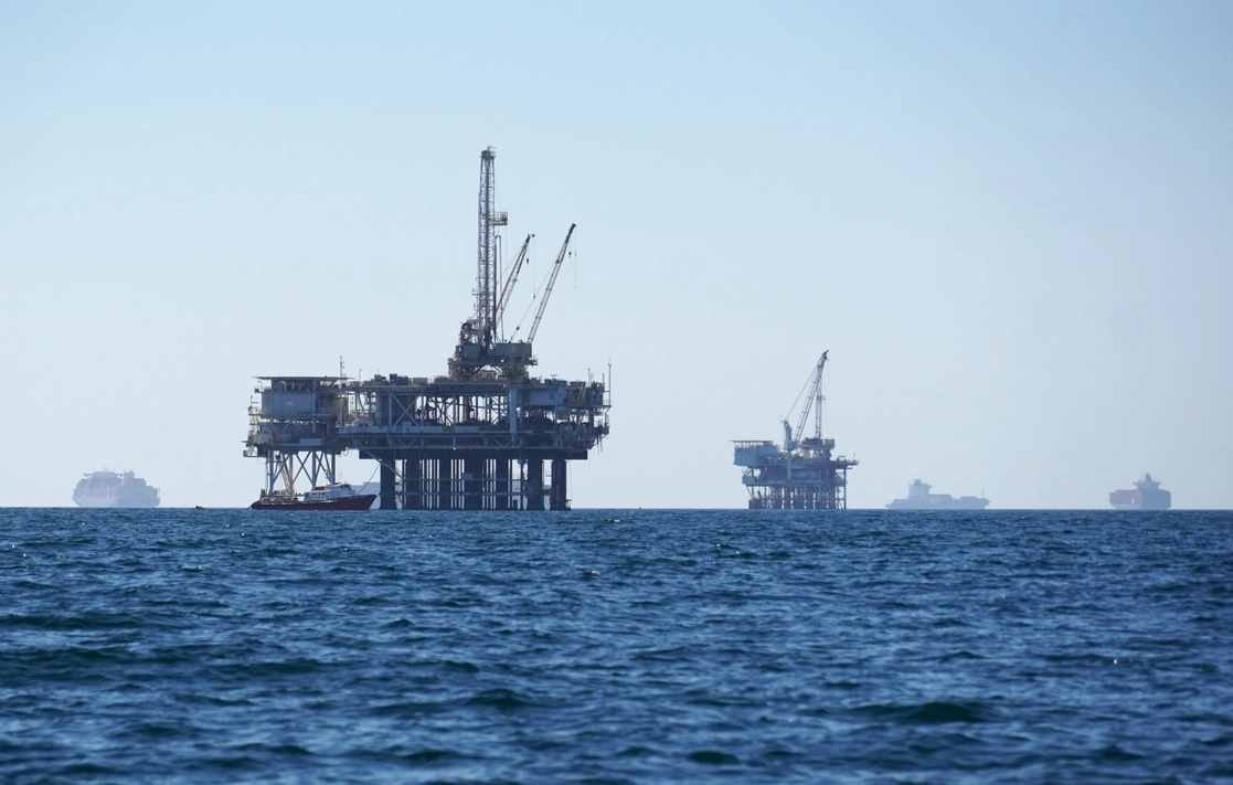 Un barco navega cerca de plataformas petroleras en altamar, antes de dirigirse al puerto de Los Ángeles-Long Beach, en EU. Foto Ap
