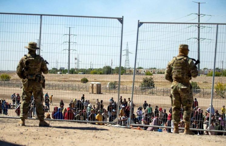 Migrantes hacen fila junto a la valla fronteriza bajo la vigilancia de la Guardia Nacional de Texas para ingresar a El Paso, el 10 de mayo pasado. Foto AP
