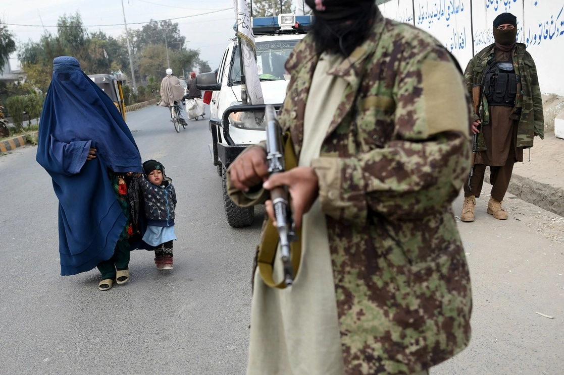 Una mujer con burka y una niña pasan junto a combatientes talibanes en una carretera de Jalalabad, Afganistán. Foto Afp / Archivo