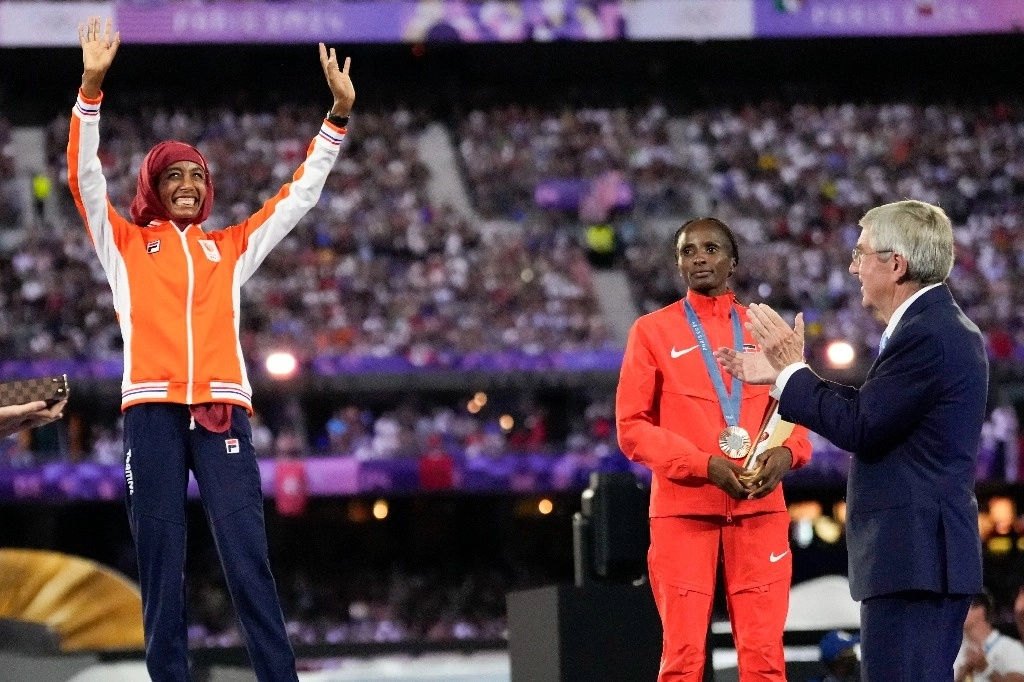 La medallista de oro en maratón femenino Sifan Hassan, de los Países Bajos, reacciona mientras el presidente del COI, Thomas Bach, se prepara para entregarle su medalla durante la ceremonia de clausura de los Juegos Olímpicos de Verano de 2024 en el Stade de France, el 11 de agosto de 2024, en Saint-Denis, Francia. Foto Ap