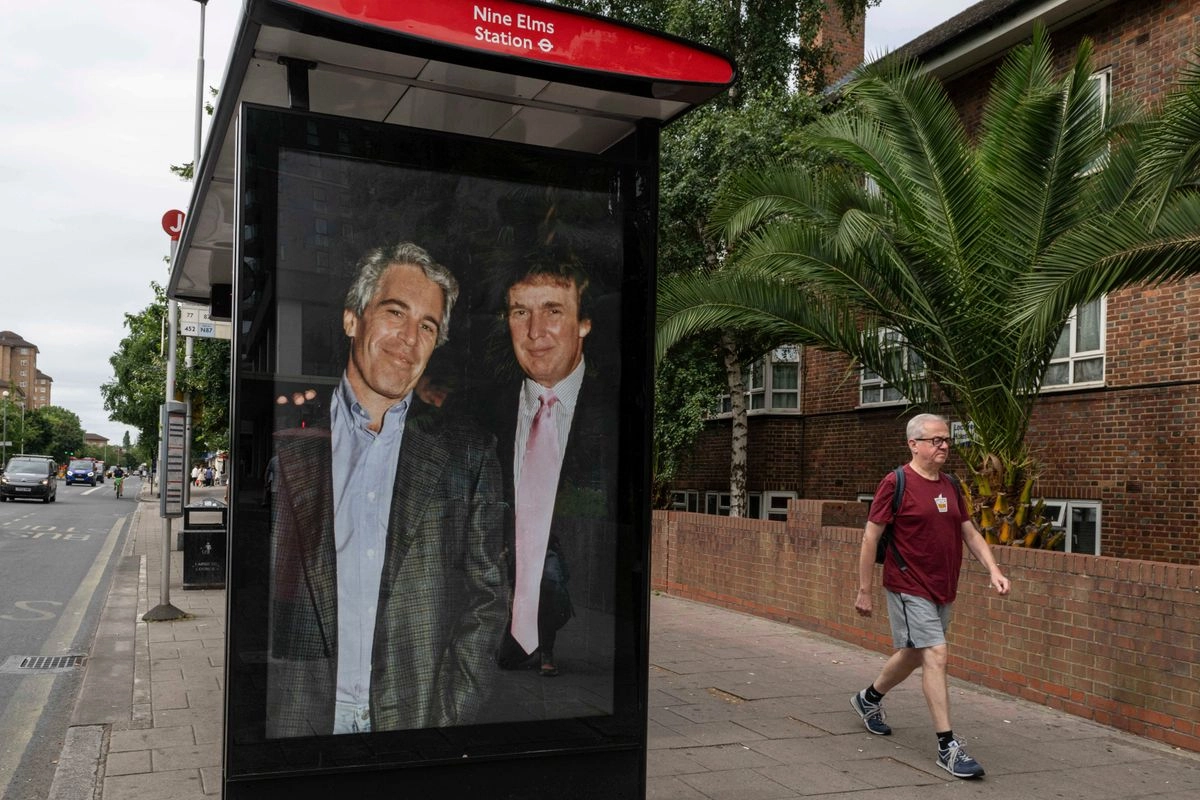 Los pasajeros pasan junto a una parada de autobús cerca de la estación Nine Elms mientras activistas colocan un cartel que muestra al presidente Donald Trump y a Jeffrey Epstein cerca de la embajada de Estados Unidos en Londres, el jueves 17 de julio de 2025. Foto 