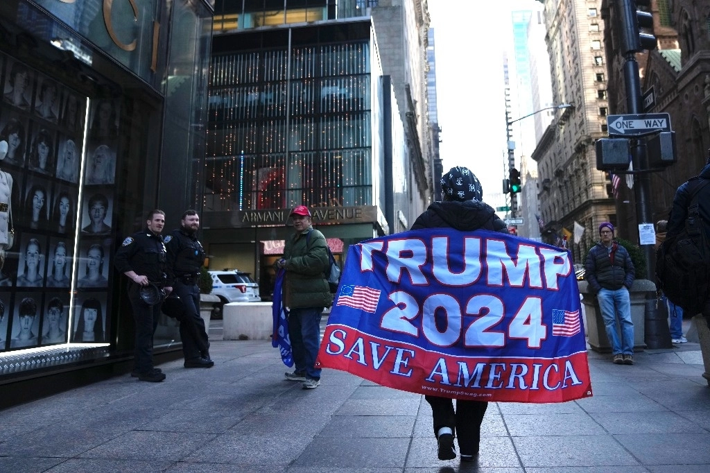 Una mujer camina por la Quinta Avenida con una bandera que muestra su apoyo al expresidente Donald Trump, el martes 21 de marzo de 2023, en Nueva York. Foto Ap