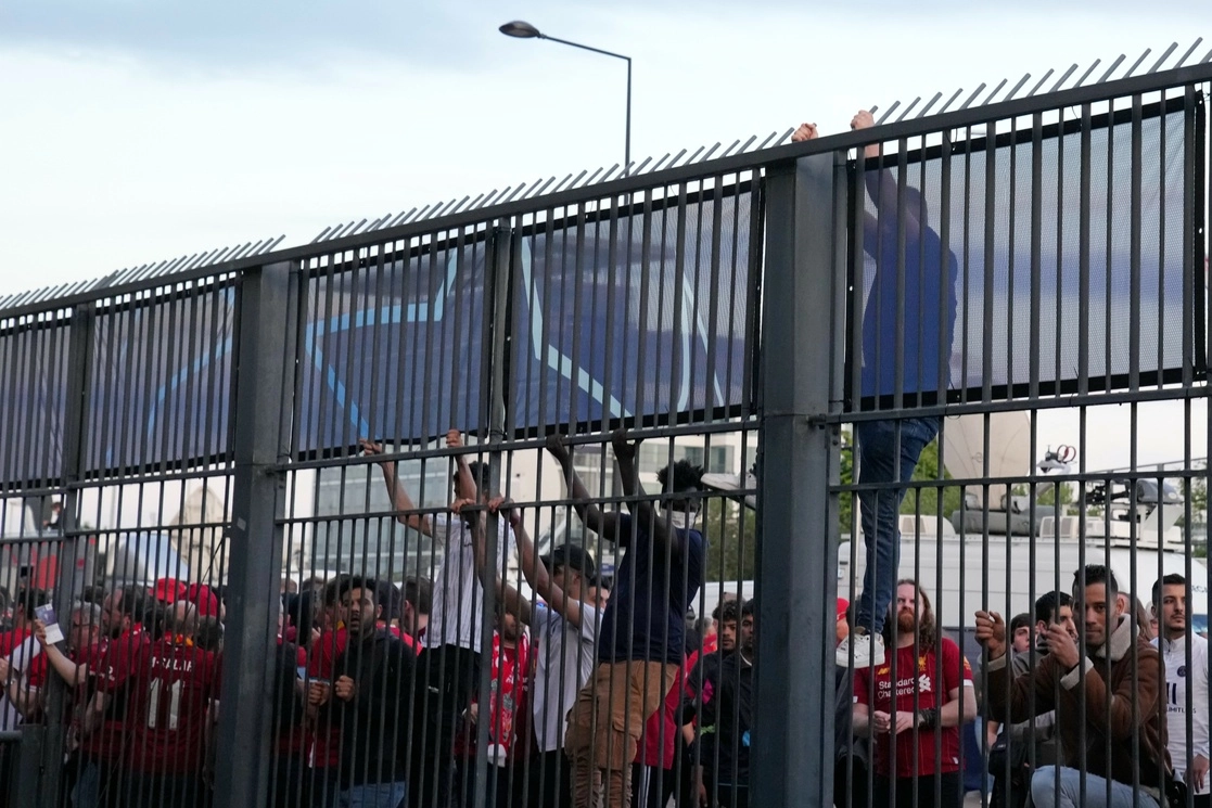Aficionados se suben a la valla frente al Stade de France antes del partido de futbol  de la final de la Liga de Campeones entre Liverpool y Real Madrid, en Saint Denis, cerca de París, el sábado 28 de mayo de 2022. La policía lanzó gases lacrimógenos contra los simpatizantes que esperaban en largas filas para ingresar al estadio. Foto Ap