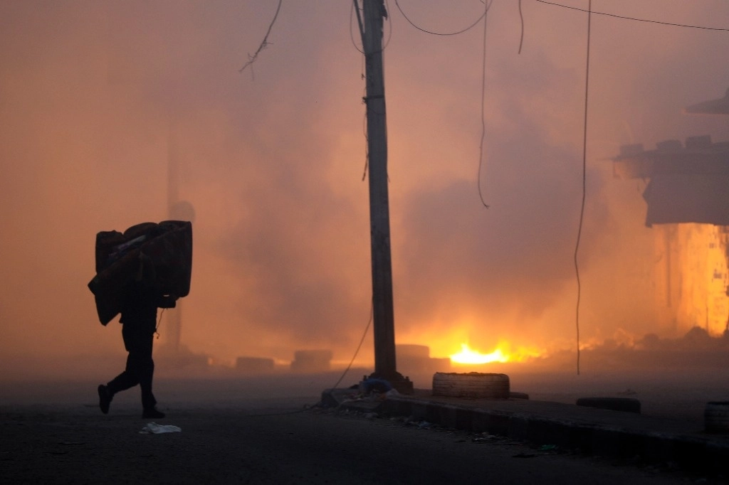 Un palestino avanza con sus pertenencias al hombro al escapar del barrio Naser, tras un bombardeo aéreo israelí en Gaza. Foto Ap