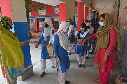 Maestras de una escuela en Lahore, Pakistán, reciben a sus alumnos con gel antibacterial y toma de temperatura. Foto Afp