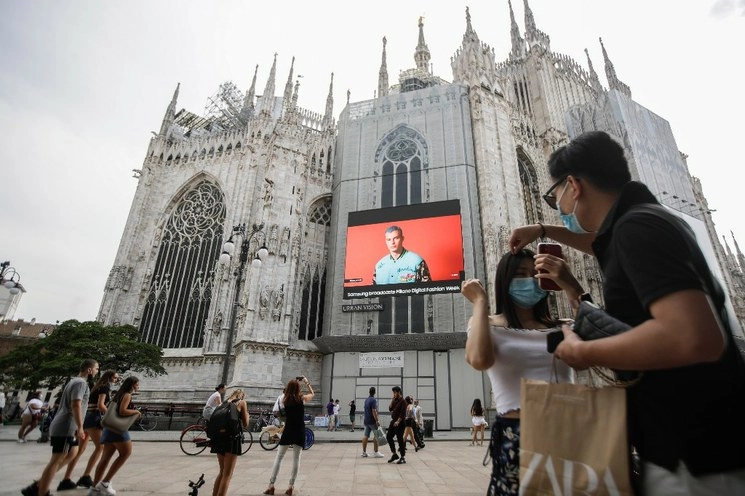 Transeúntes pasan debajo de una pantalla instalada en la Catedral del Duomo, ubicada en Milán, muestra a una modelo de Moschino, durante la Semana de la Moda Digital de Milán, Italia, el 14 de julio de 2020. Foto Ap