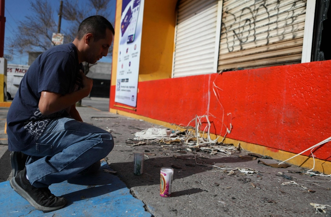 Un hombre coloca una veladora en la tienda Rapiditos Bip-Bip, en la colonia Infonavit Juárez Nuevo, en Ciudad Juárez. Foto Afp